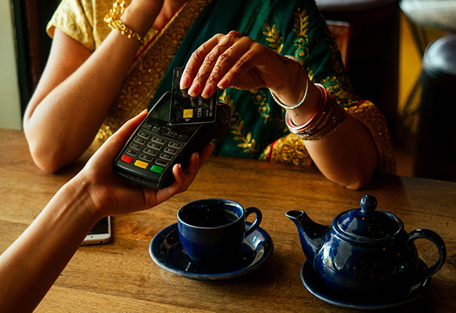 Indian businesswoman in green traditional sari using payment terminal with a credit card in a cafe restaurant