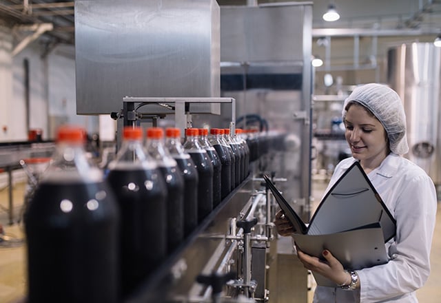 Happy female worker in bottling factory writing notes about bottles before shipment
