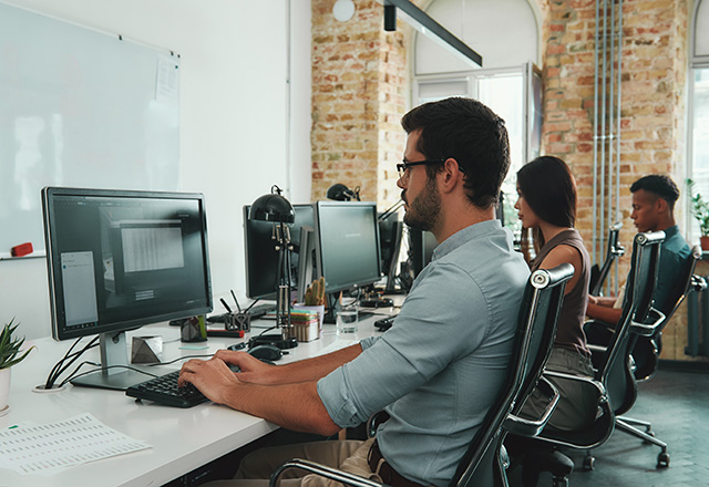 Side view of young busy employees working on computers while sitting at desk in modern open space