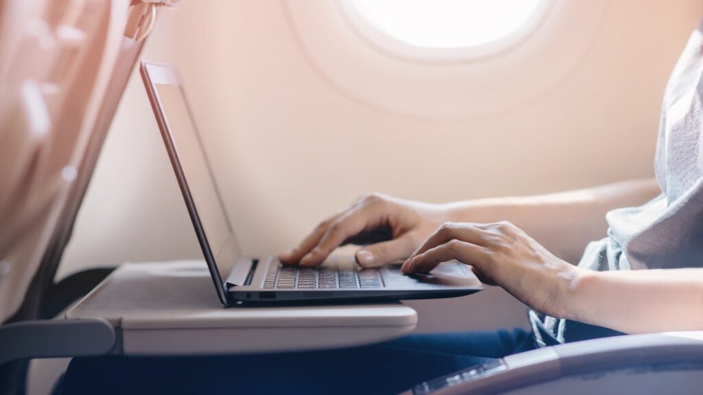 Woman using laptop on airplane for workforce access.